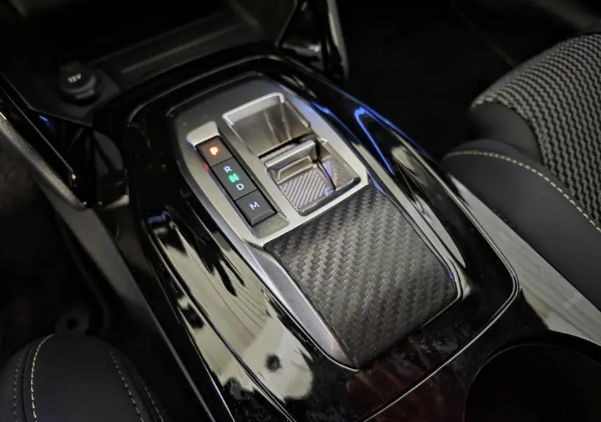 Gros plan sur la console centrale noire brillante avec sélecteur de boîte automatique et surpiqûres vertes du siège tissu Peugeot 208 GT blanc.