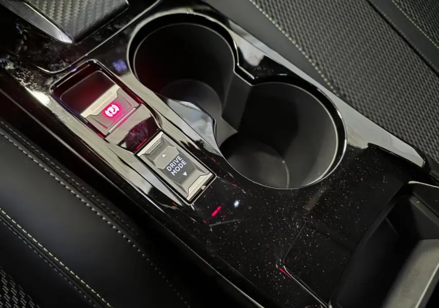 Gros plan sur la console centrale noire brillante avec bouton Drive Mode et frein à main électrique du Peugeot 208 blanc.