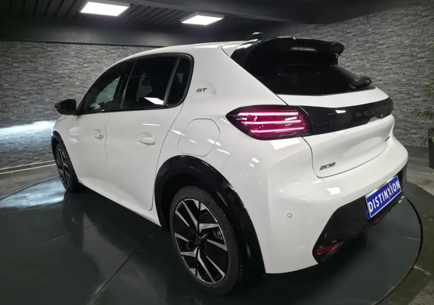 Vue 3/4 arrière droite d'une Peugeot 208 GT blanche avec jantes alliage bi-ton et feux arrière LED allumés.