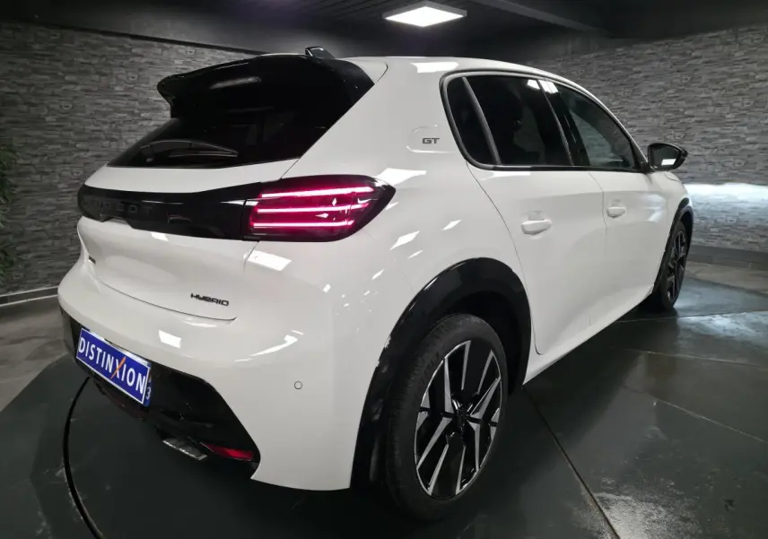 Vue 3/4 arrière droite d'une Peugeot 208 blanche hybride avec jantes alliage bi-tons et feux arrière LED distinctifs.