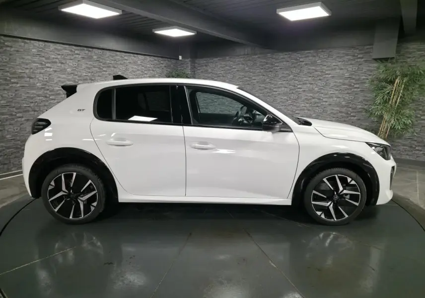 Profil droit d'une Peugeot 208 blanche 2025 GT avec jantes alliage bi-tons et élargisseurs d'ailes noirs brillants.