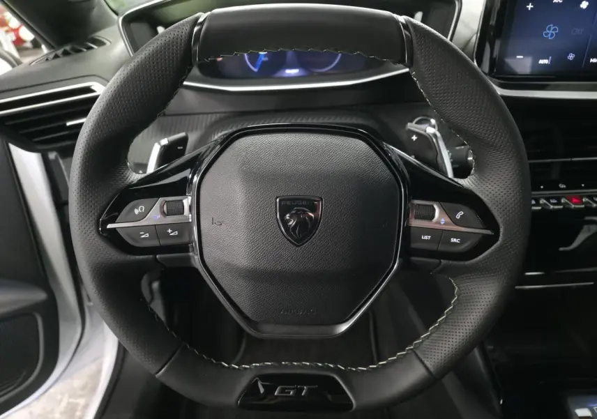 Volant cuir noir perforé avec badge GT au centre, vue rapprochée de l’habitacle de la Peugeot 208 blanche 2025.