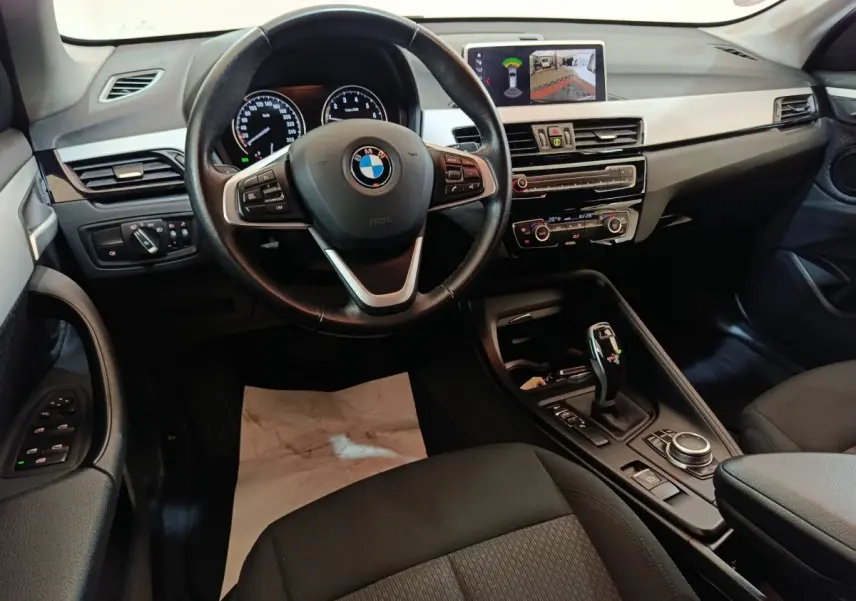 Intérieur BMW X1 sDrive18i 2021 vu de face, tableau de bord noir avec écran multimédia et volant cuir multifonctions.