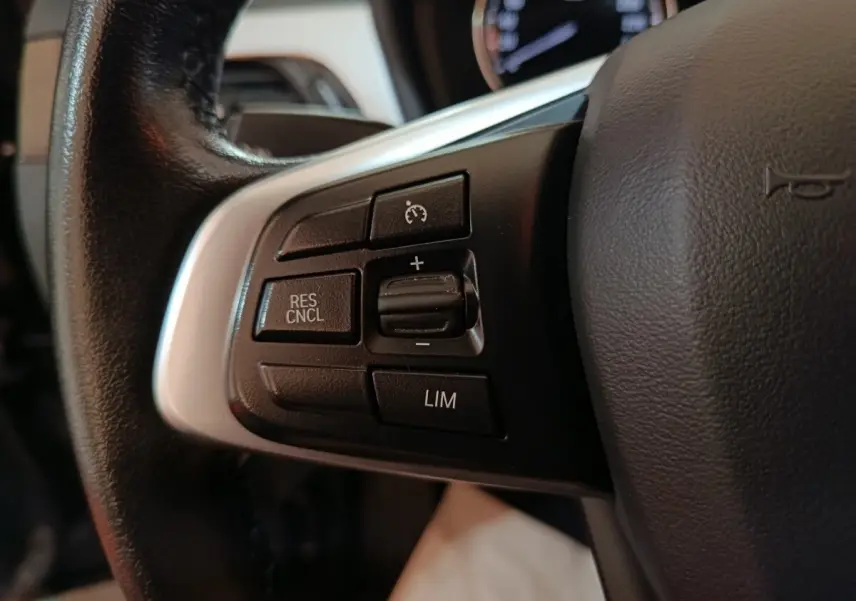 Gros plan sur les commandes du régulateur de vitesse au volant cuir noir d’un BMW X1 gris foncé 2021.