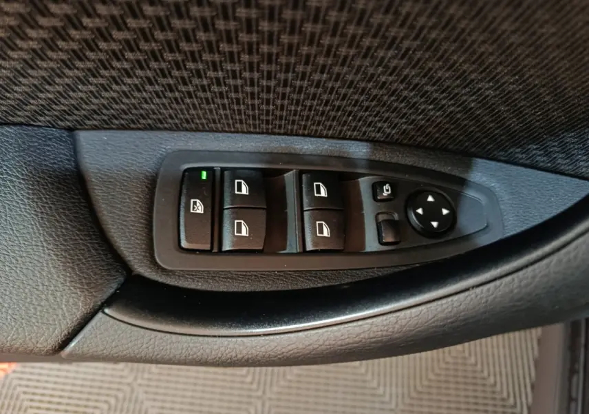 Gros plan sur les commandes de lève-vitres et rétroviseurs côté conducteur en plastique noir dans une BMW X1 gris foncé.