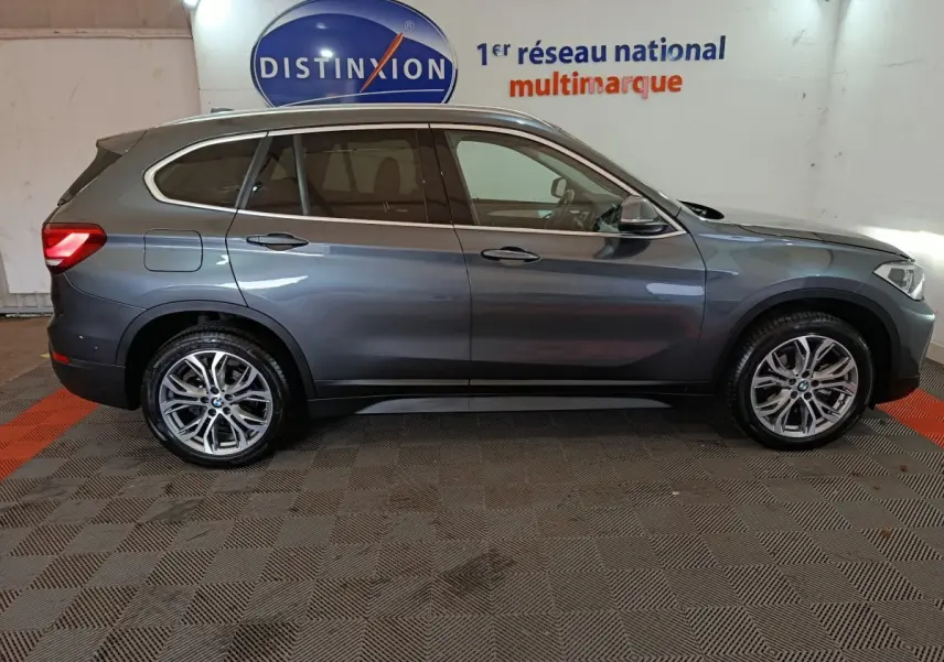 BMW X1 sDrive18i Lounge gris foncé vue de profil côté gauche, avec jantes alliage et vitres teintées, en intérieur showroom.