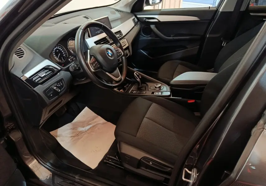 Vue intérieure côté conducteur du BMW X1 gris foncé, montrant le volant cuir multifonctions et la console centrale moderne.