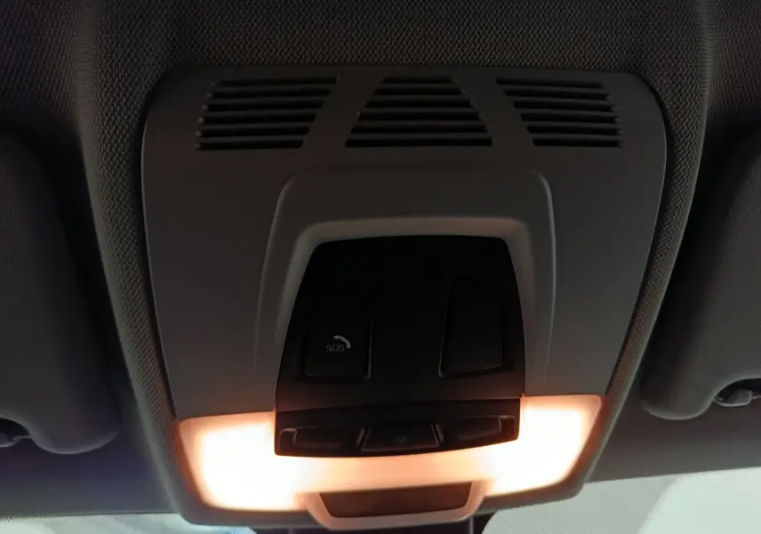 Vue intérieure en gros plan du plafonnier avec boutons SOS et éclairage allumé dans un BMW X1 gris foncé 2021.