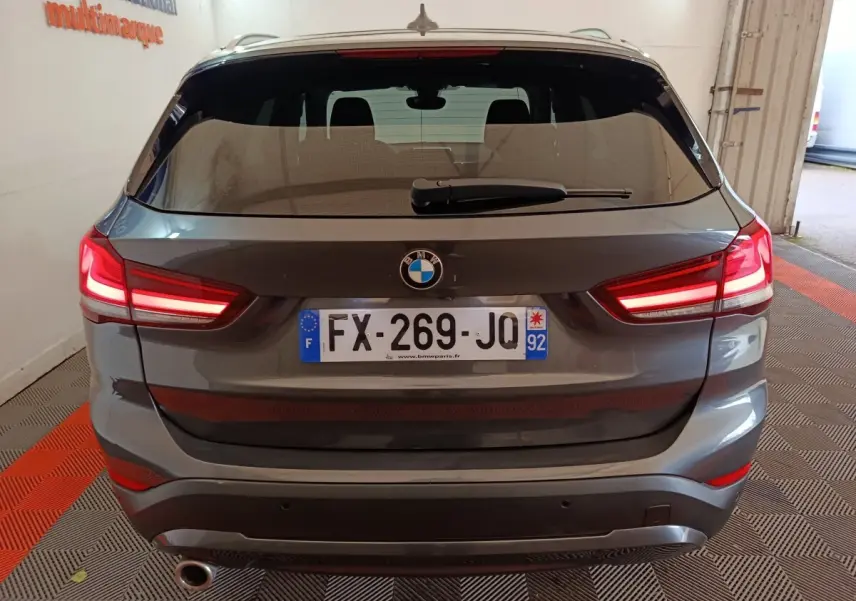 Vue arrière d’un BMW X1 gris foncé avec feux arrière allumés et plaque d’immatriculation française visible.