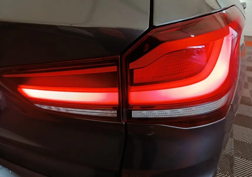 Gros plan sur le feu arrière droit rouge vif d’un BMW X1 sDrive18i Lounge gris foncé, avec carrosserie brillante.