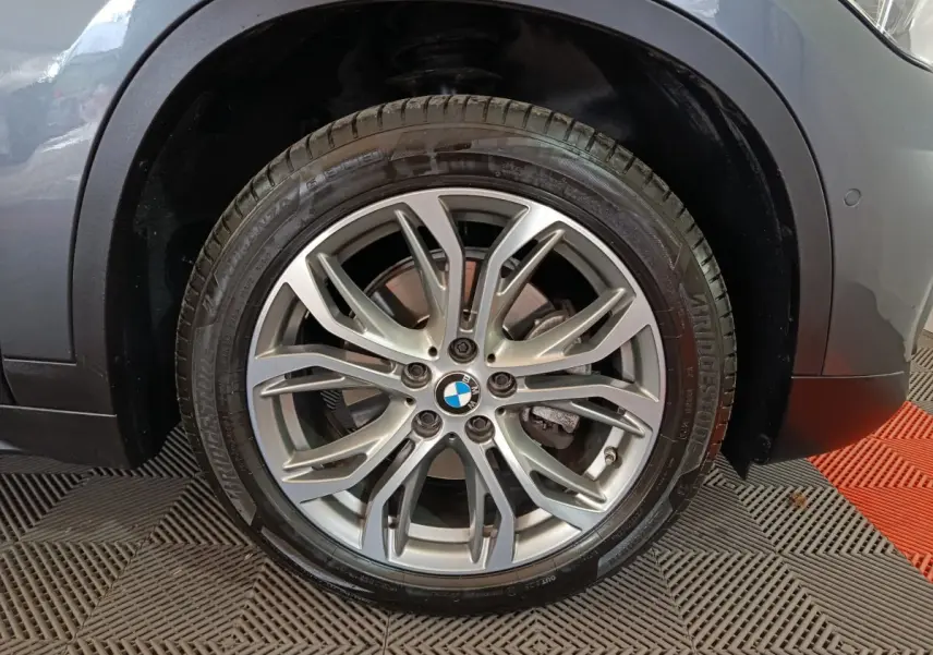 Gros plan sur la roue avant droite d’un BMW X1 gris foncé, mettant en valeur la jante alliage et le logo BMW central.