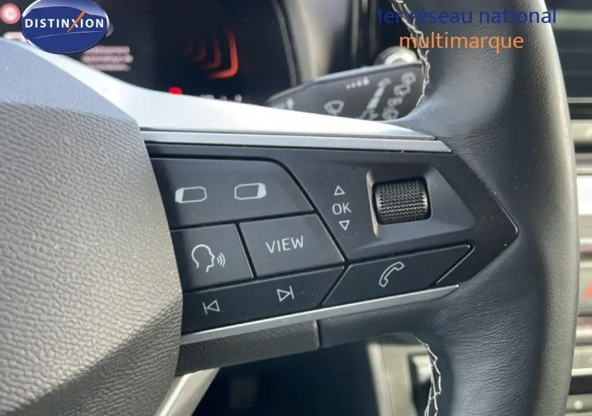 Gros plan sur les commandes gauche du volant en cuir noir du SEAT Ibiza bleu Fjord 2025, avec boutons multifonctions.