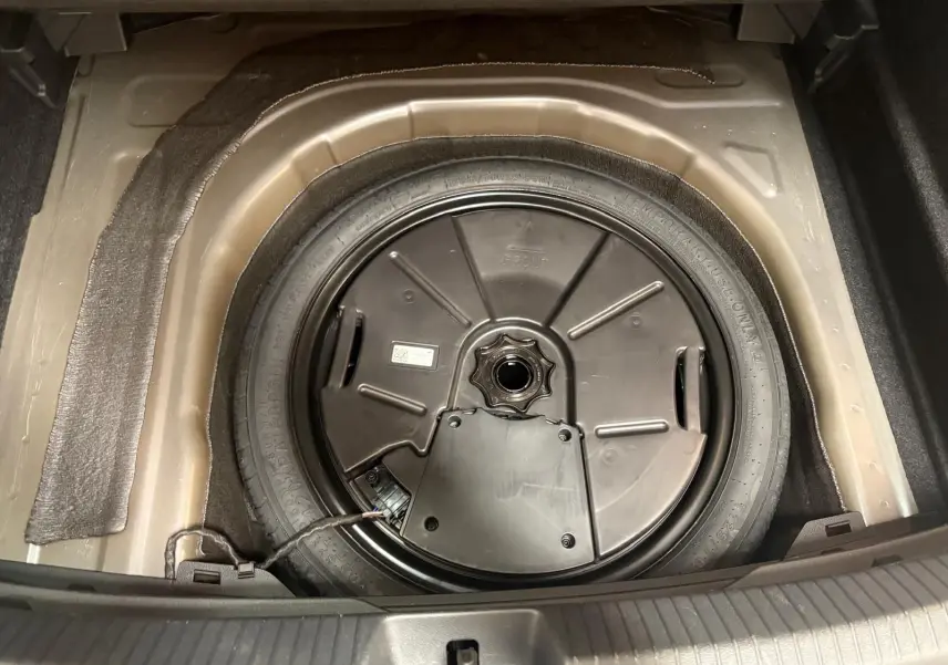 Gros plan sur la roue de secours compacte du Volkswagen Taigo 2024, logée dans le coffre, avec son cache noir circulaire.