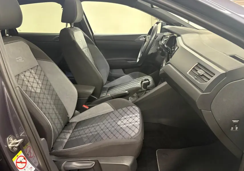 Vue intérieure côté gauche du Volkswagen Taigo 1.5 TSI R-Line 2024, sièges avant en tissu gris à motifs et volant visible.