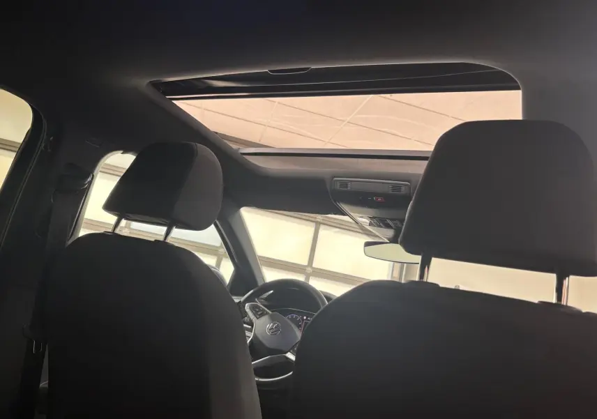 Vue intérieure depuis l'arrière montrant le toit ouvrant en verre et le volant du Volkswagen Taigo gris cendré 2024.