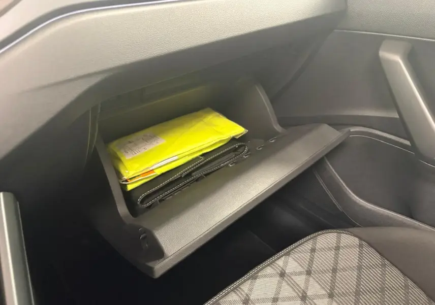 Vue intérieure du coffre à gants ouvert côté passager du Volkswagen Taigo gris cendré, avec documents jaunes visibles.