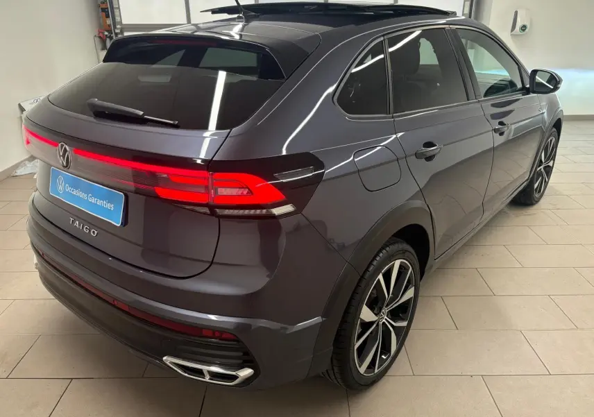 Vue 3/4 arrière droite du Volkswagen Taigo gris cendré avec jantes noires brillantes et toit ouvrant en verre.