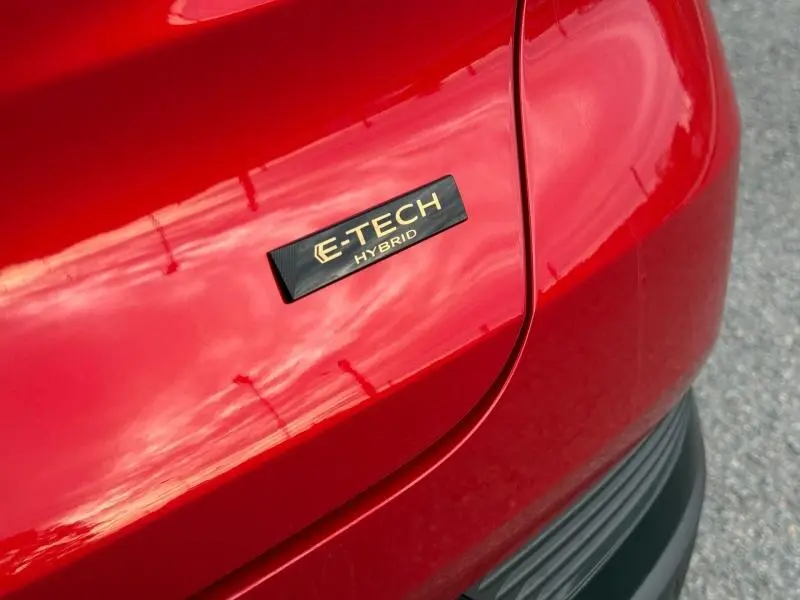 Gros plan sur l’inscription E-TECH Hybrid en doré sur la carrosserie rouge flamme arrière du Renault Captur.