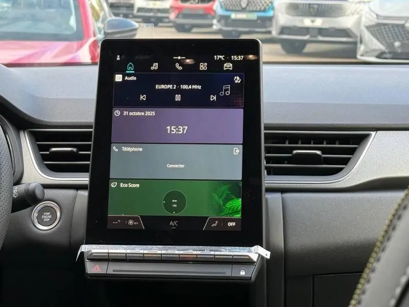 Vue intérieure centrée sur l'écran tactile vertical du tableau de bord du Renault Captur rouge 2025, avec bouton start/stop visible.
