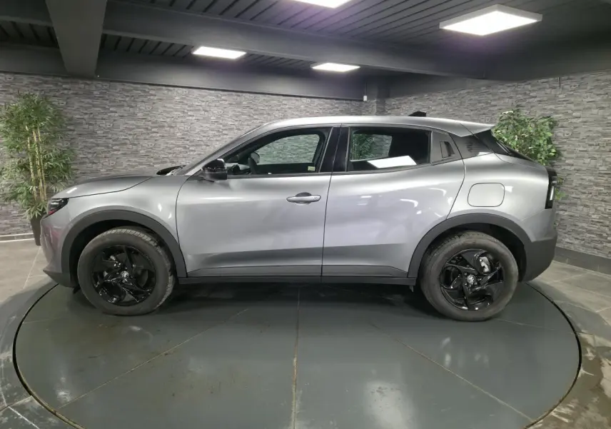 Vue de profil côté gauche d'une Alfa Romeo Junior 1.2 Ibrida grise avec jantes alliage noires dans un showroom.