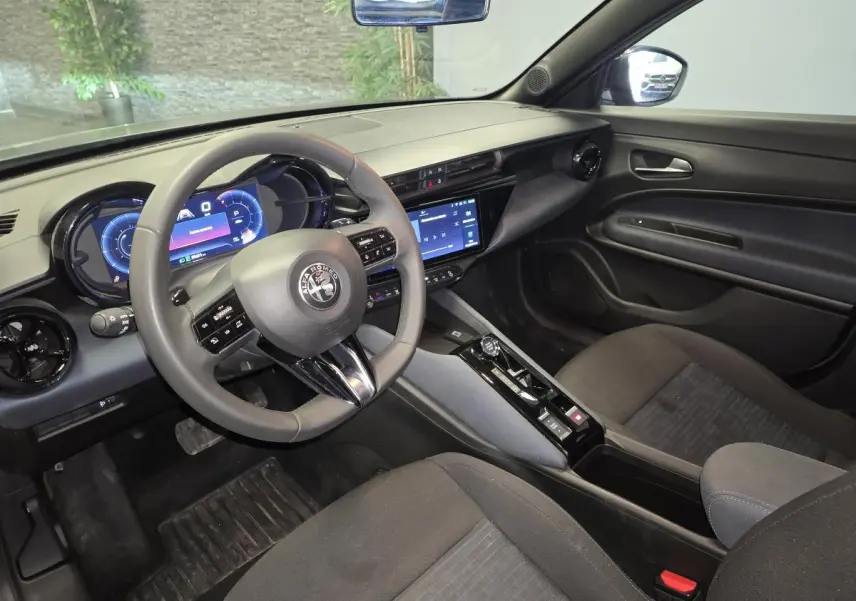 Vue intérieure côté conducteur de l'Alfa Romeo Junior 1.2 hybride 2025 avec tableau de bord digital et sellerie Icona grise.