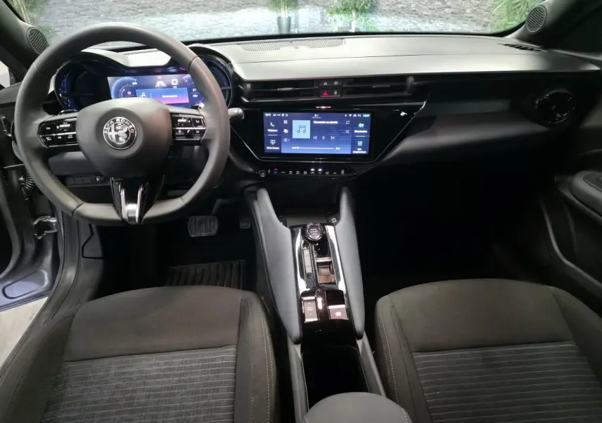 Vue intérieure avant de l'Alfa Romeo Junior 1.2 Ibrida gris, avec tableau de bord digital et écran tactile central.