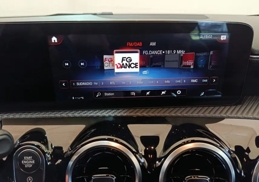 Gros plan sur l’écran tactile multimédia et les aérateurs ronds noirs du tableau de bord d’une Mercedes Classe A noire.