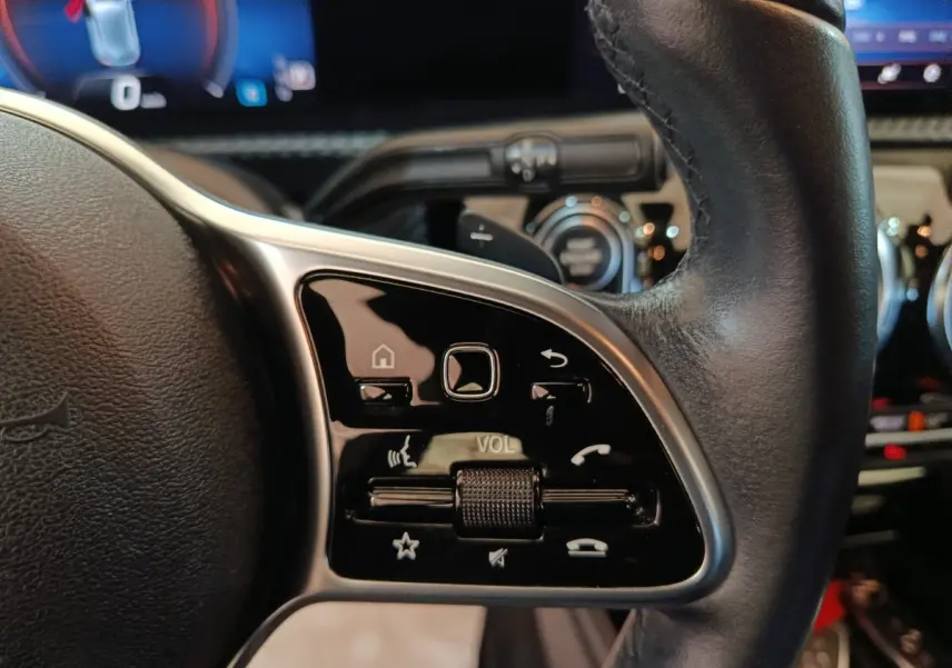 Gros plan sur les commandes multifonctions noires du volant cuir côté gauche de la Mercedes Classe A noire 2021.
