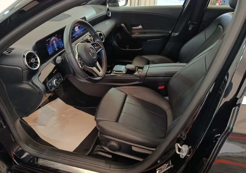 Vue intérieure côté conducteur de la Mercedes Classe A 200 Business Line noire, avec tableau de bord digital et sièges cuir noirs.