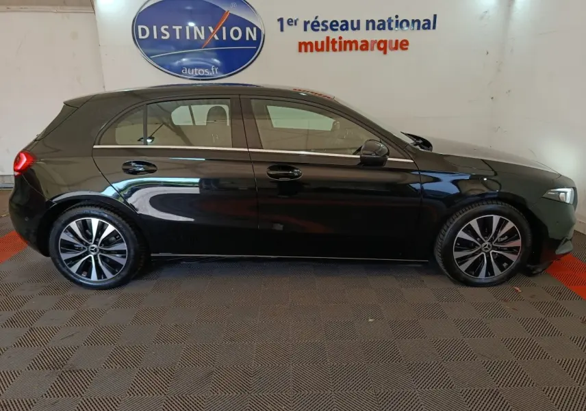 Profil latéral droit de la Mercedes Classe A 200 Business Line noire, avec jantes alliage et toit spoiler visible en intérieur showroom.