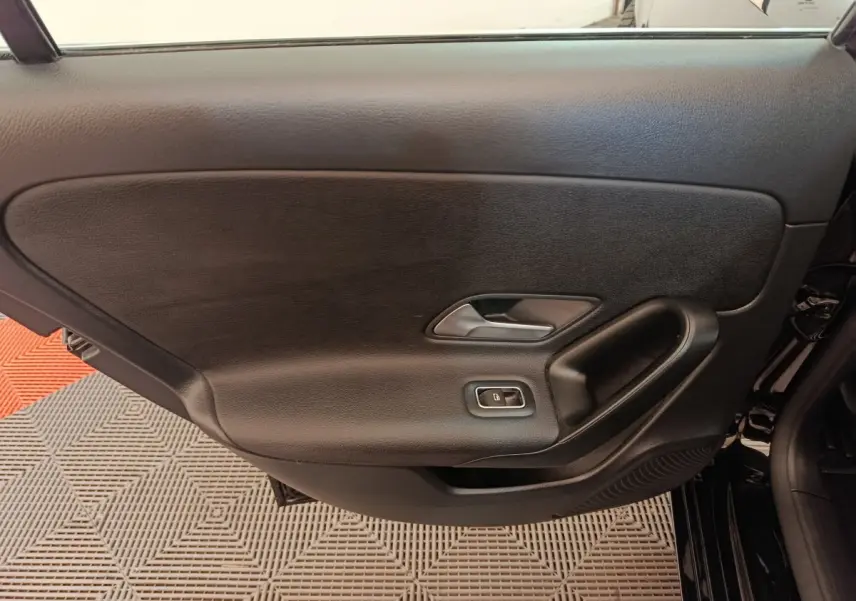 Vue intérieure côté gauche de la porte noire d'une Mercedes Classe A 200 Business Line 2021 avec poignée et commande de fenêtre.
