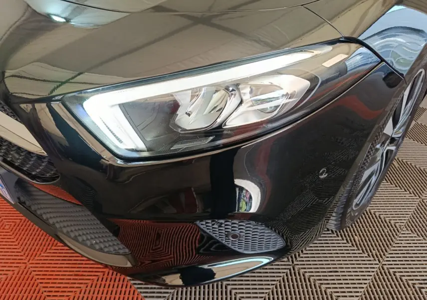 Gros plan sur le phare avant droit noir brillant de la Mercedes Classe A 200 Business Line 2021 avec jante visible.