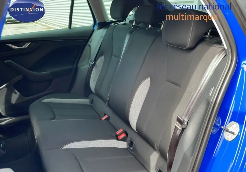 Vue intérieure côté arrière droit de la Skoda Scala 2025 en bleu Racing Metal, sièges tissu gris et noir avec ceintures visibles.