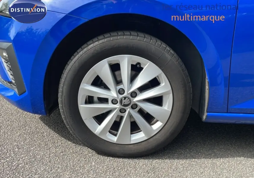 Gros plan sur la roue avant gauche d'une Skoda Scala bleu racing metal, avec jante argentée à plusieurs branches.