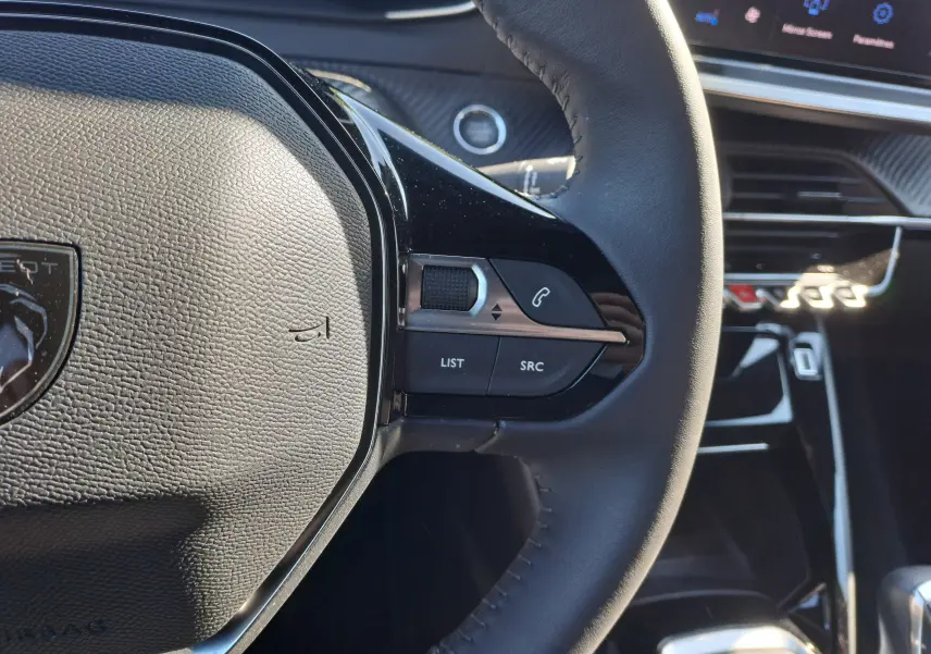 Gros plan sur le volant côté droit du Peugeot 2008 Rouge Elixir 2023, avec commandes audio et écran tactile en arrière-plan.