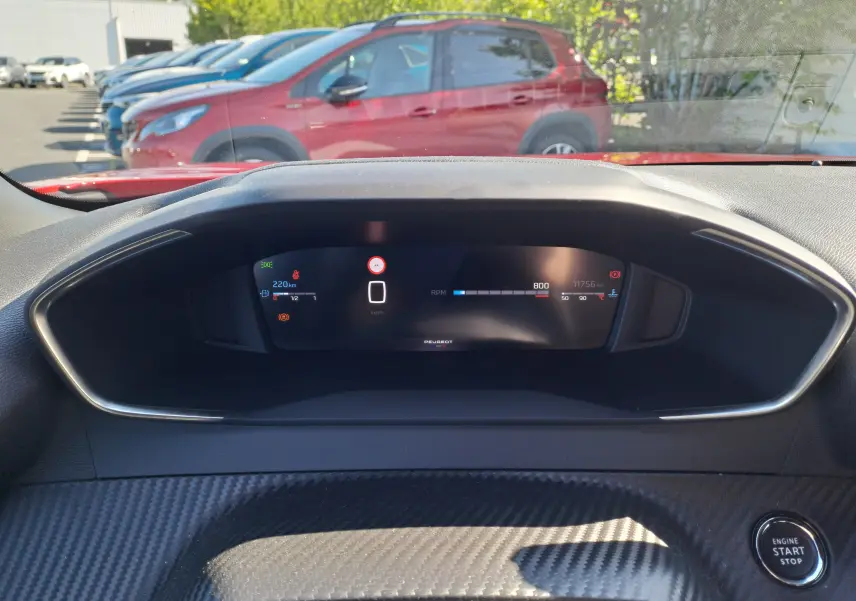Vue depuis l'habitacle du tableau de bord numérique du Peugeot 2008 rouge Elixir, avec bouton start/stop visible.