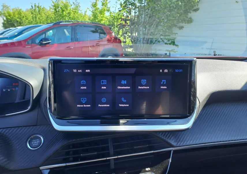 Vue intérieure du tableau de bord avec écran tactile du Peugeot 2008 rouge Elixir visible à travers le pare-brise côté gauche.