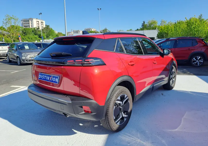 Vue 3/4 arrière droite d'un Peugeot 2008 1.2 PureTech 100 Allure rouge Elixir avec toit noir et jantes alliage.