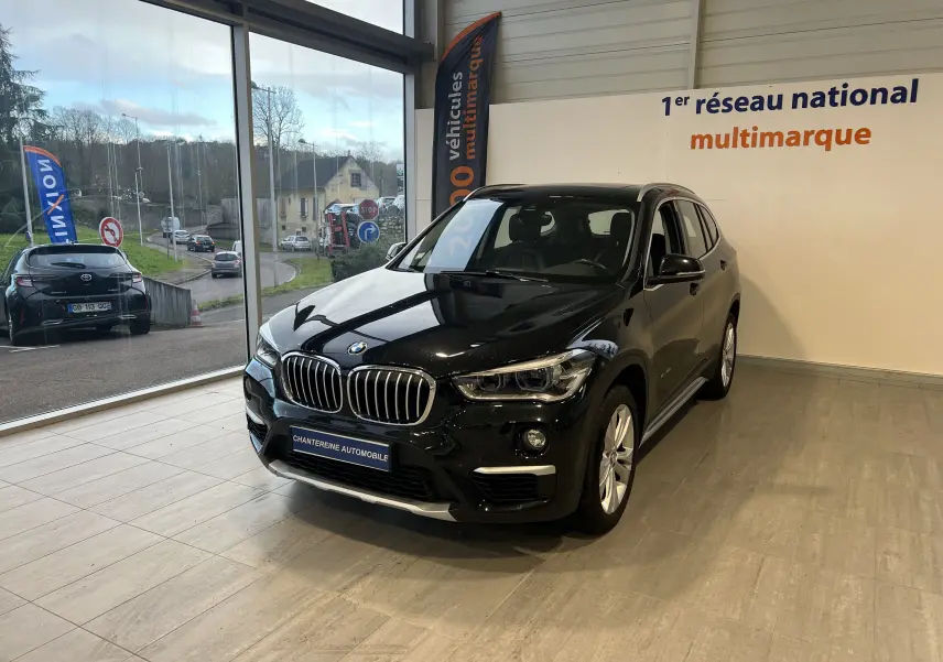 BMW X1 F48 Saphirschwarz en 3/4 avant droit, SUV compact diesel exposé en showroom lumineux.
