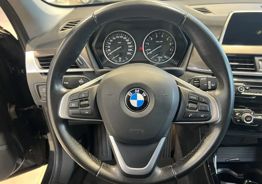 Vue rapprochée du volant en cuir noir de la BMW X1 F48 2017 avec tableau de bord et commandes intégrées visibles.
