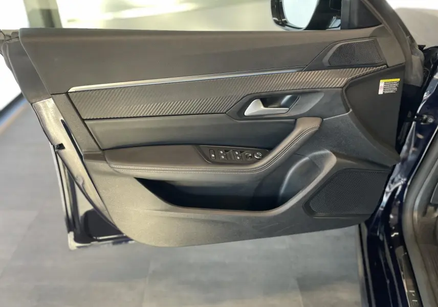 Vue latérale du panneau de porte avant gauche en cuir noir et inserts carbone du Peugeot 508 SW bleu foncé.
