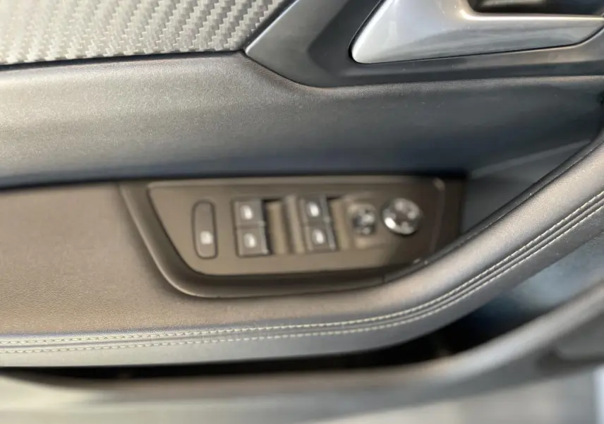 Gros plan sur les commandes de lève-vitres et rétroviseurs côté conducteur d'une Peugeot 508 SW bleu foncé.