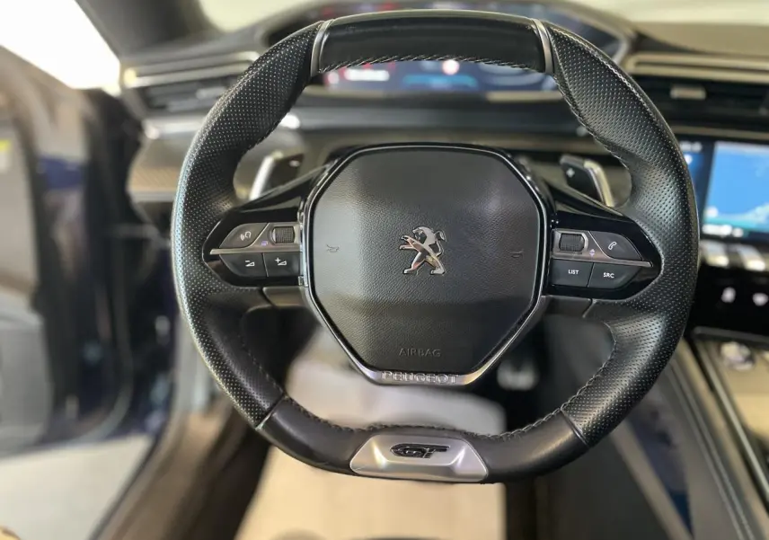 Volant noir perforé avec logo Peugeot et badge GT, vue frontale de l'intérieur du break 508 SW bleu foncé.