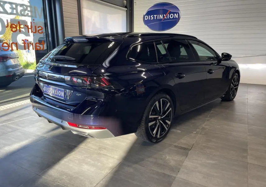 Peugeot 508 SW bleu foncé vue 3/4 arrière droit en intérieur avec jantes alliage et logo GT visible.