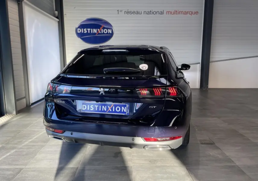 Vue arrière d'une Peugeot 508 SW bleu foncé avec feux arrière allumés et logo GT visible en intérieur showroom.