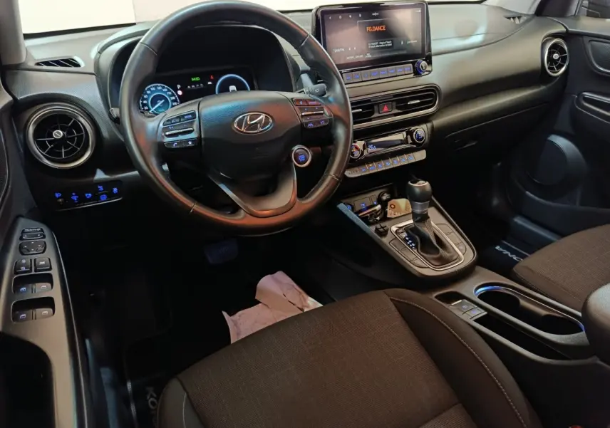 Vue intérieure avant droite du Hyundai Kona 1.6 Hybrid 2023, volant cuir multifonctions et écran tactile central allumé.