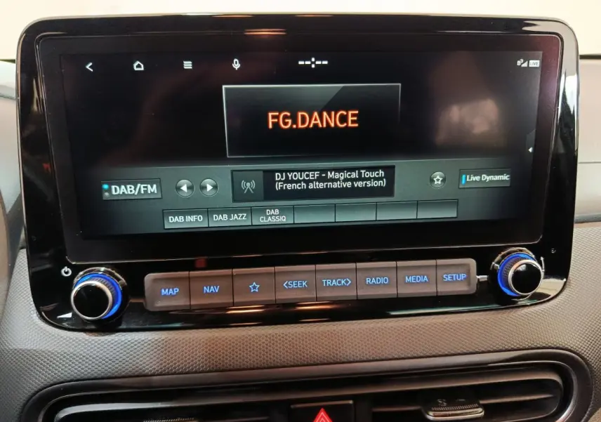 Écran tactile central du tableau de bord du Hyundai Kona gris foncé, affichant une radio DAB/FM avec commandes en dessous.