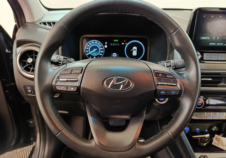 Vue intérieure centrée sur le volant cuir multifonctions du Hyundai Kona 1.6 Hybrid 2023 avec tableau de bord digital.