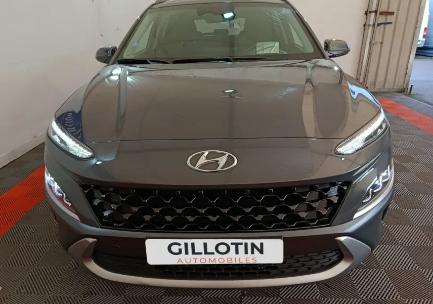 Vue avant d’un Hyundai Kona gris foncé 2023 avec calandre noire et feux LED allumés dans un garage.