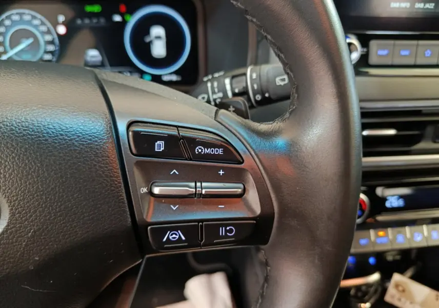 Gros plan sur le volant cuir multifonctions du Hyundai Kona 2023, avec commandes de régulateur et affichage numérique en arrière-plan.